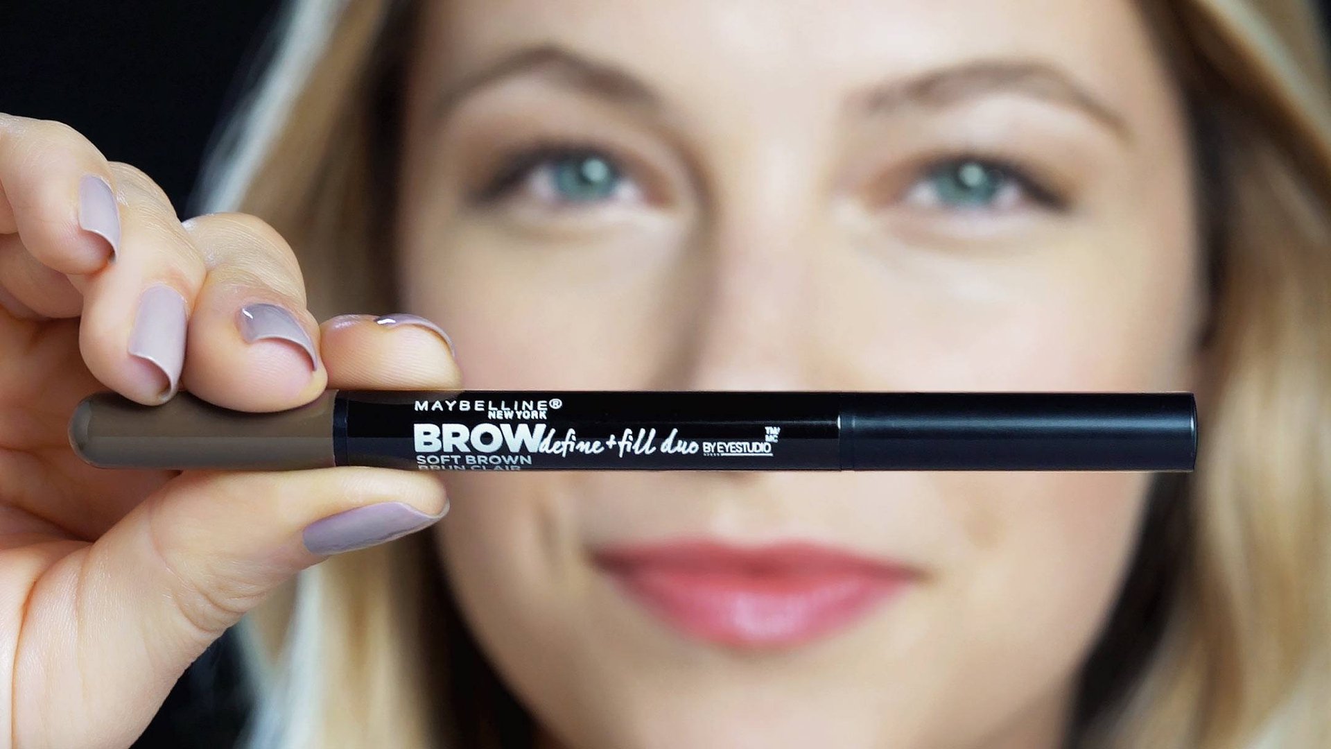 Focus op een Maybelline Brow Define and Fill Duo-product, vastgehouden door een blonde vrouw 
